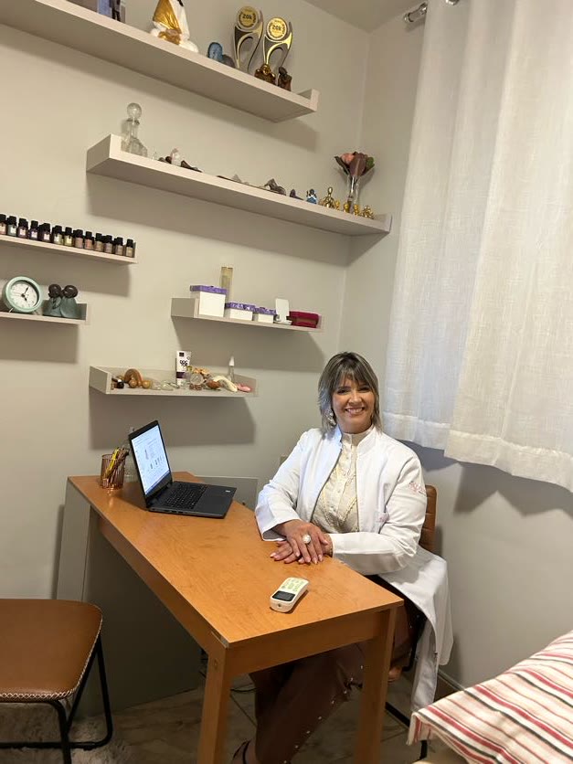 Juliana acolhendo na mesa do consultório, prateleiras com cristais ao fundo